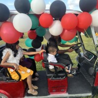 man giving kids a golf cart ride decorated with balloons