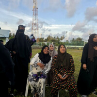 group of middle aged Thimarafushi woman on a grass field. woman on right singing the Maldivian national anthem
